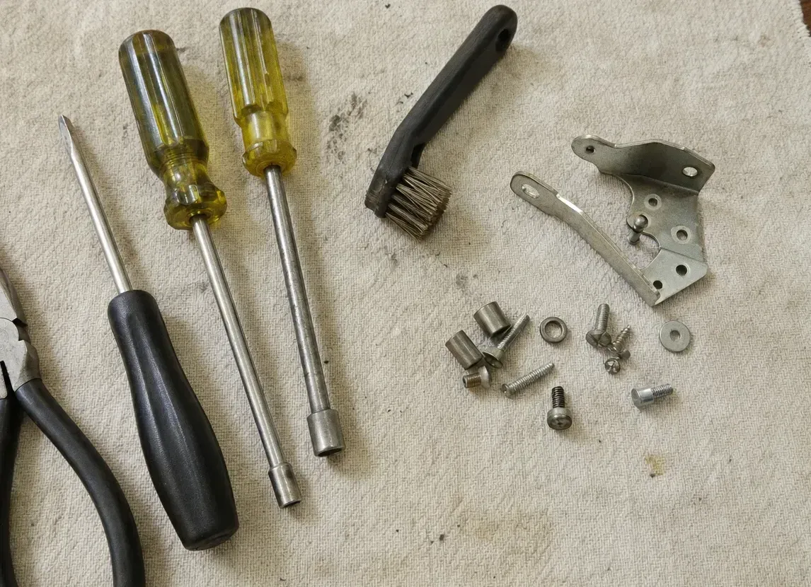 Screwdrivers, a nut driver, a wire brush and a small bracket laid out on a canvas cloth with loose screws